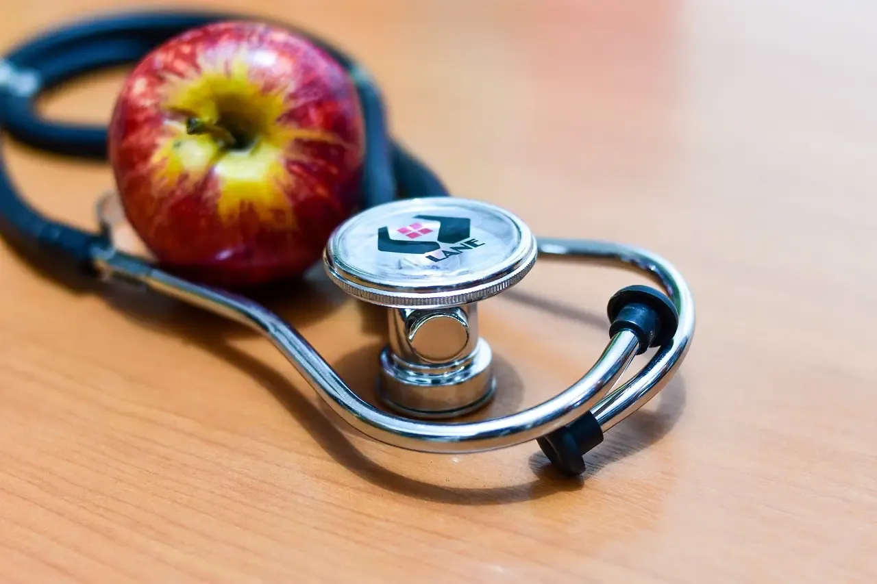 Apple resting next to a stethoscope on a wooden table