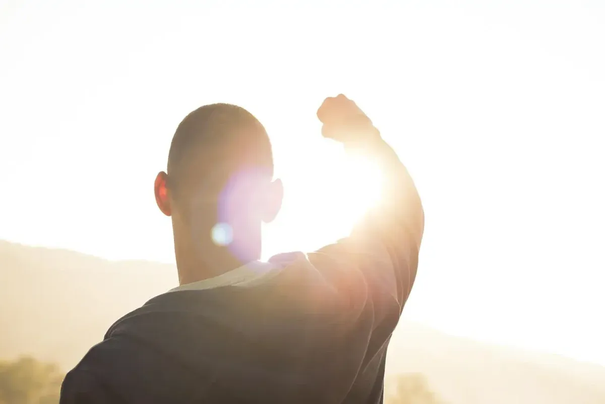 Person celebrating with arms raised against a glowing sky