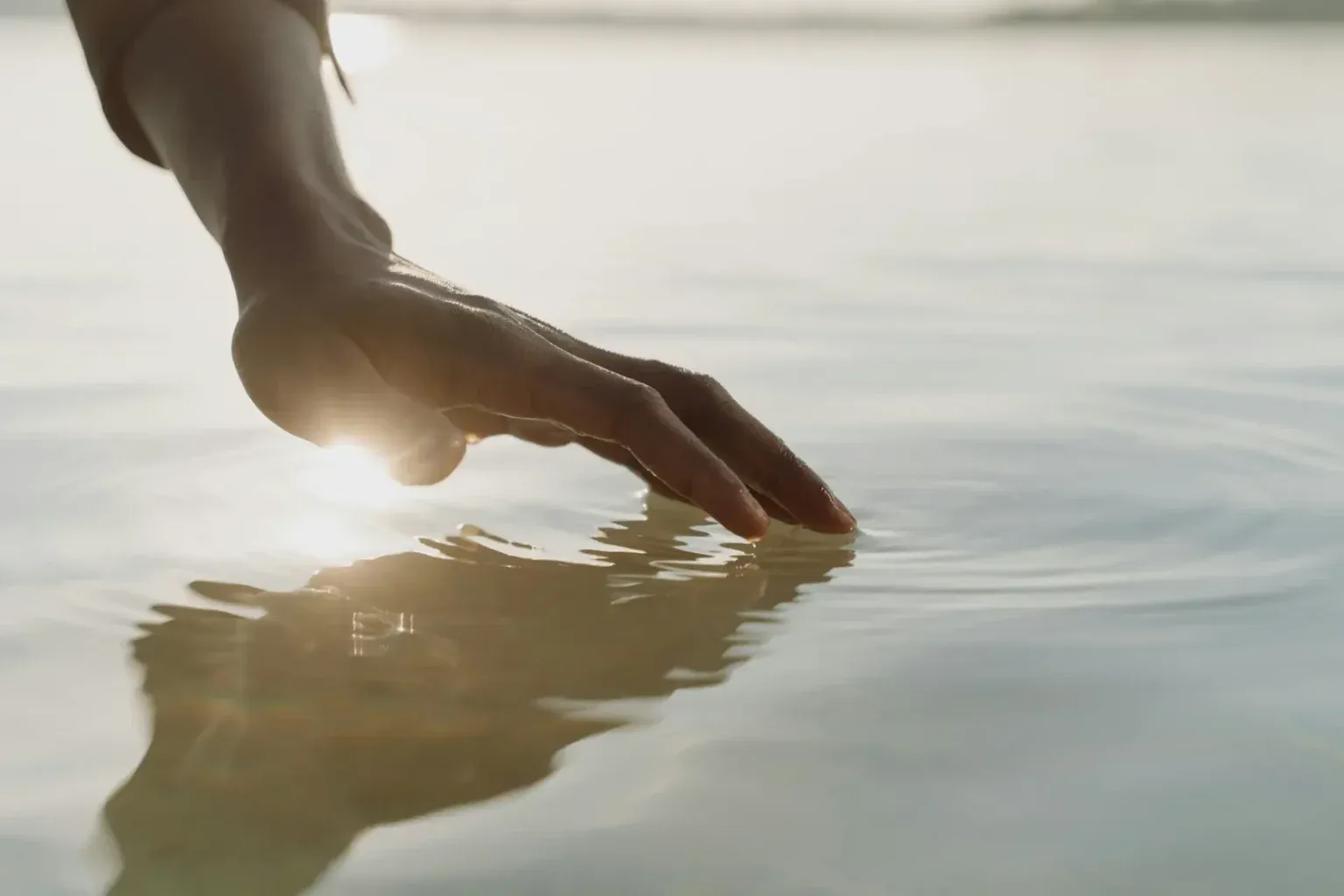 A hand resting on the surface of still water