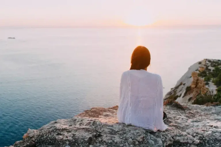 Woman in white sitting by the ocean at sunrise