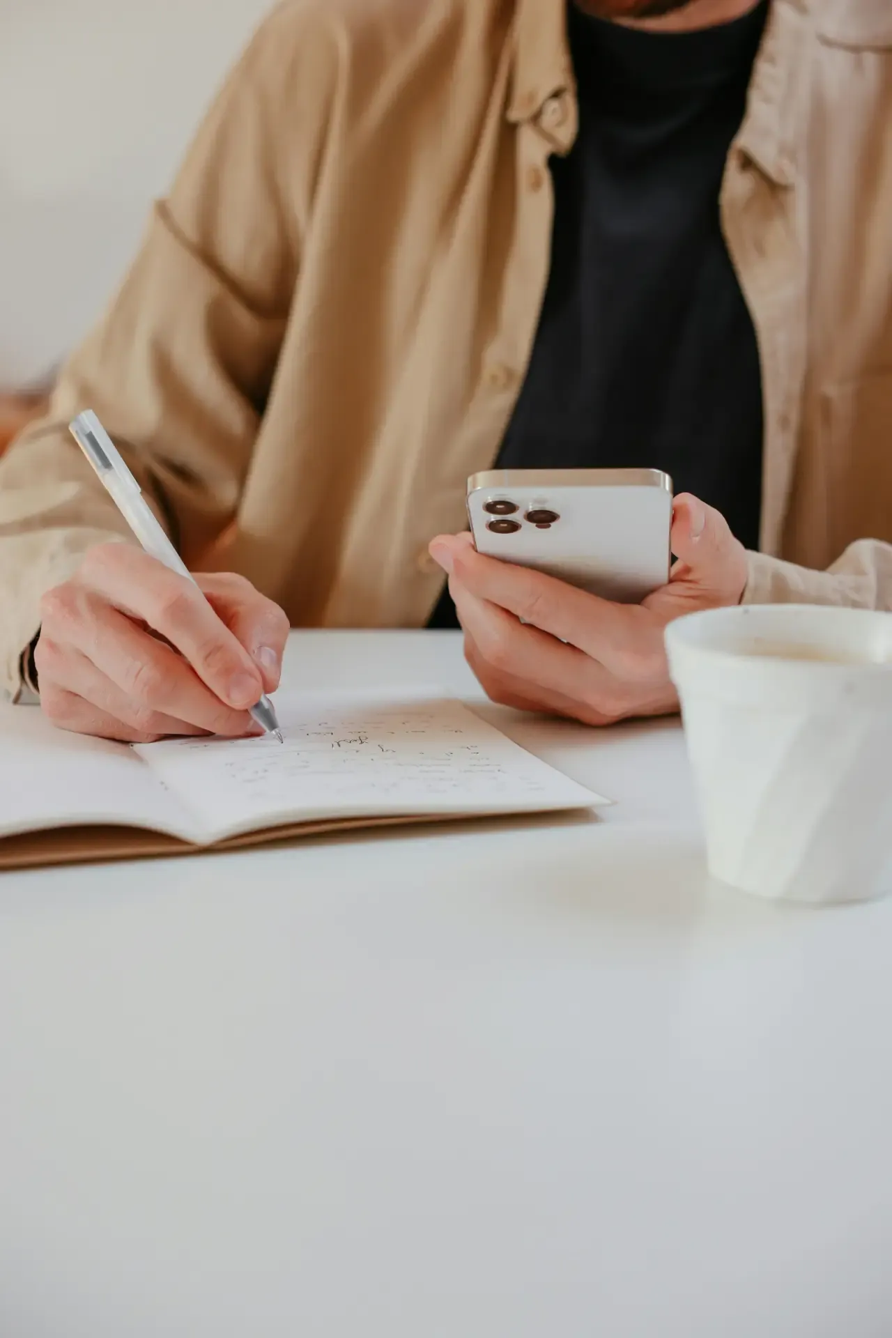 Person writing in a journal with phone in hand