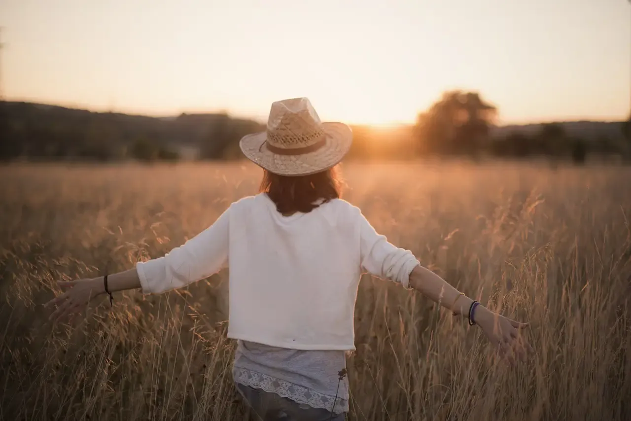 Person standing in a sunlit field with arms gently outstretched