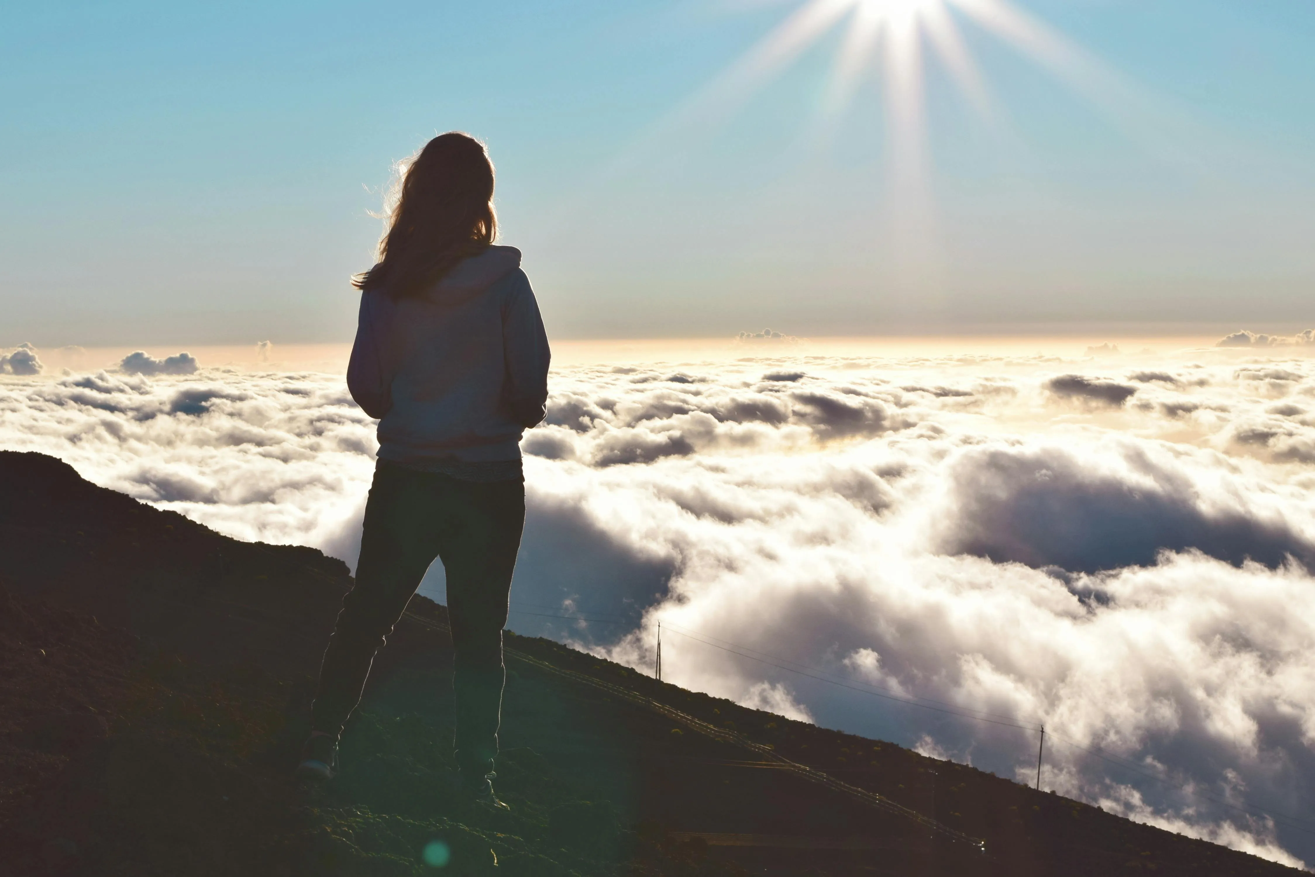 Woman standing above the clouds looking toward the light